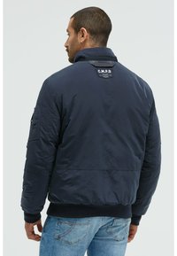 Marineblaue Bomberjacke aus glattem, leichtem Stoff. Verfügt über einen gestrickten Saum, Reißverschlusstaschen und ein Logopatch auf der Rückseite.