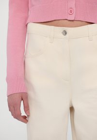 Light pink fitted cardigan with a ribbed cuff paired with cream-colored denim pants featuring front pockets and a button closure.