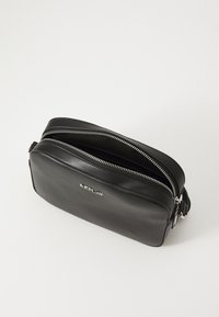 Svart skinn crossover-bag med doble glidelåser, en glatt overflate og en sølvlogo aksent på forsiden. Har en strømlinjeformet rektangulær form.