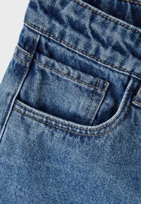 Jeans de mezclilla con un lavado azul, costuras visibles y un bolsillo trasero con un borde superior curvado. La textura muestra un patrón de sarga clásico.