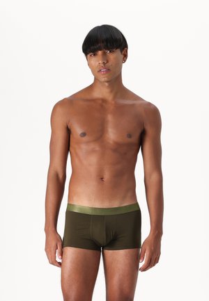 Ελιές πράσινα σλιπ με σατέν φινίρισμα στη μέση, κατασκευασμένα από μαλακό, ελαστικό ύφασμα που αγκαλιάζει το σώμα χωρίς ορατές ραφές.