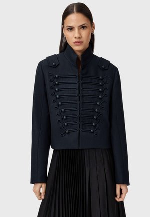 Marineblaue Wolle Militärjacke mit hohem Kragen, dekorativem Kordelverschluss an der Vorderseite und Schulterklappen. Maßgeschneiderte, cropped Passform.