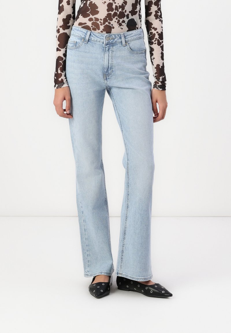 Ljusblå raka jeans med medelhög midja, tillverkade av denim, med en klassisk femficksdesign. Bärs med svarta spetsiga ballerina skor.