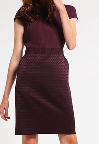 Robe à manches courtes en bordeaux sombre, dotée d'un panneau texturé sur la jupe avec un motif subtil et une silhouette ajustée.