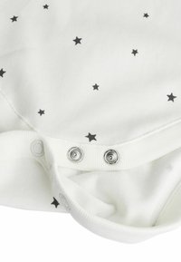 Body blanc avec imprimé étoiles noires. Présente des boutons-pression en métal argenté en bas. Tissu en coton doux avec col et poignets côtelés.
