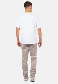 Weißes Baumwoll-T-Shirt und hellbeige Hose, mit schmaler Passform, sichtbaren Nähten und Gesäßtaschen. Schuhe sind weiß mit schwarzen Akzenten.