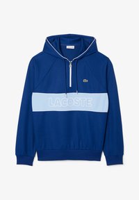 Blå hettegenser laget av mykt stoff med frontglidelås, hvite detaljer og en stor "LACOSTE" logo i lyseblå over brystet.