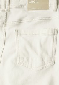 Vita bomulljeans med en stickad bakficka, där varumärkesetiketten "Cecil" finns ovanför. Slät textur och standard femfickdesign.