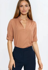 Jasnobrązowa bluzka z dekoltem w serek, krótkie rękawy podwinięte, wykonana z gładkiej tkaniny, w połączeniu z ciemnogranatowymi, dopasowanymi spodniami.