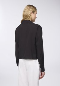 Blazer nero cropped con maniche lunghe, texture liscia e colletto a revers. Abbinato a pantaloni bianchi, che mostrano un design semplice.