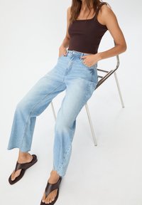 Světle modré džíny s vysokým pasem, rovnými nohavicemi a roztrhaným lemem, doplněné hnědým tílkem a hnědými žabkami.