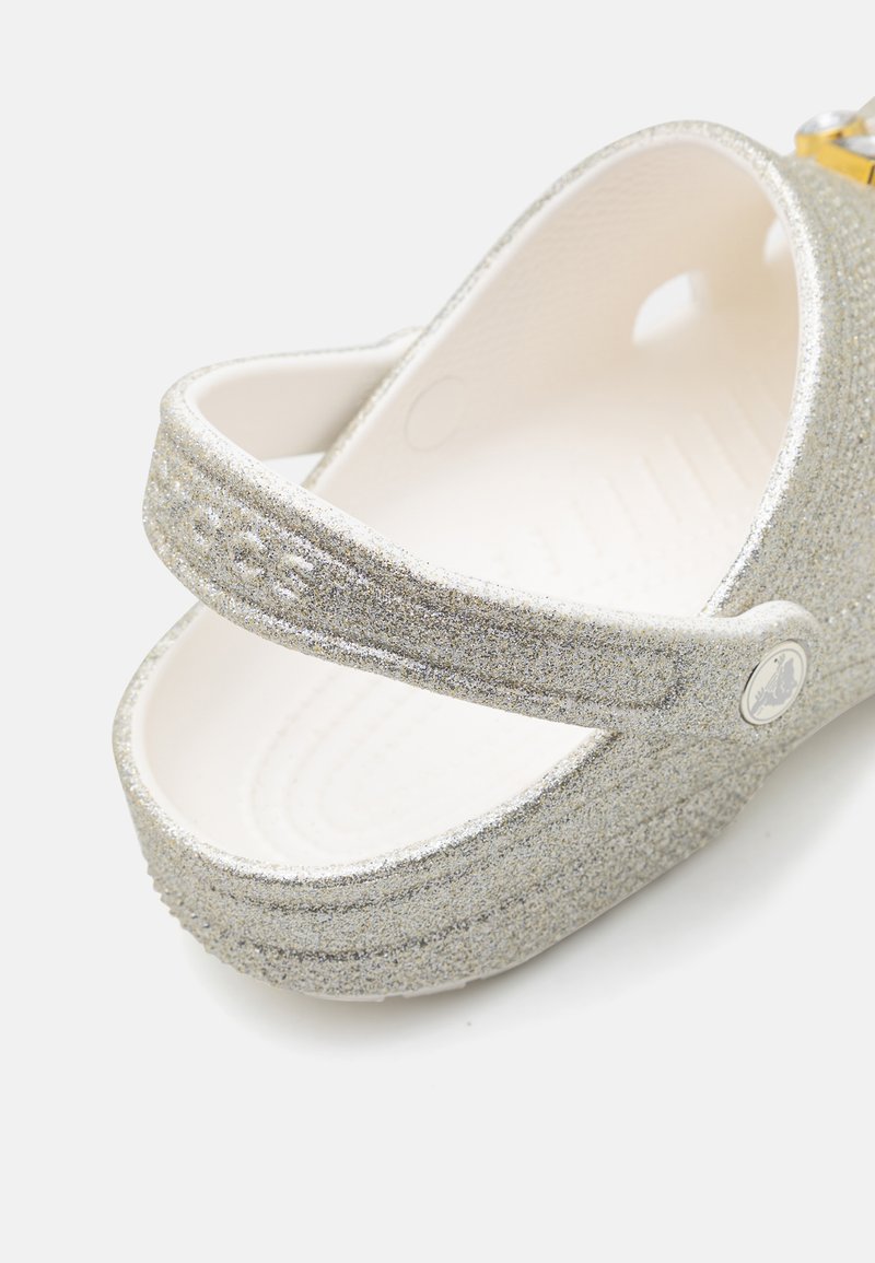 Silberne Glitzer-Clogs mit einem weißen Innenraum. Zwei verstellbare Riemen und ein runder Akzent. Texturierte Oberfläche und konturiertes Fußbett.