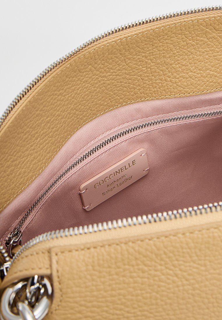 Dzeltena teksturēta ādas soma ar rozā odere un uzlīmi "Coccinelle Authentic Italian Leather." Redzams rāvējslēdzēja details.