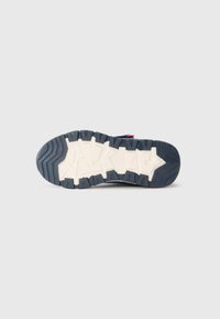 Suola scanalata di un sandalo blu scuro con motivi geometrici bianchi su uno sfondo grigio chiaro uniforme.