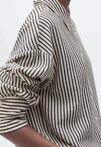 Chemise à rayures avec col boutonné, en tissu léger. Présente des rayures verticales noires et blanches et des manches retroussées.