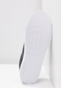 Sneaker nero con tomaia testurizzata e suola in gomma bianca. La suola presenta un motivo circolare per la presa e un logo in rilievo.