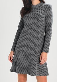 Vestido gris de manga larga con una tela texturada y con patrón. El diseño presenta un corsé ajustado y una falda acampanada, ofreciendo una silueta clásica.