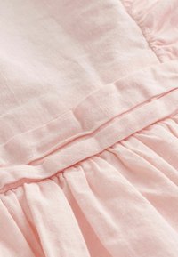 Tissu en lin rose clair avec un point de rassemblement et un détail de couture pliée créant texture et profondeur.