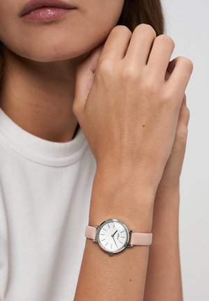 Runde Uhr mit weißem Zifferblatt und silbernen Stundenmarkierungen, ausgestattet mit einem hellrosa Lederarmband. Glatte Textur und minimalistisches Design.