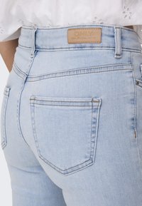 Világoskék farmernadrág magas derékkal, hátul bőr címkével és két hátsó zsebbel, melyek látható varrási részletekkel rendelkeznek.
