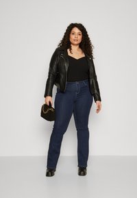Chaqueta de motorista de cuero negro sobre un body negro de canalé, combinada con jeans rectos de mezclilla azul oscuro y un bolso negro texturizado con cadena dorada.