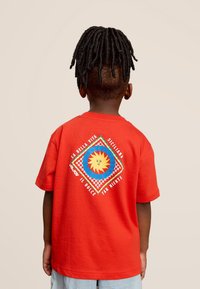 Rode T-shirt met korte mouwen, voorzien van een kleurrafische print met een zon en geometrische patronen. Zacht katoen materiaal, ontspannen pasvorm.