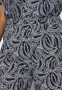 Námořnický overal s bílým vzorem listů, elastickým pasem, krátkými rukávy a hladkou texturou.