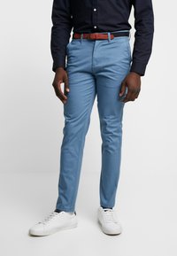 Světle modré chinos kalhoty s úzkým střihem, vyrobené z hladké bavlny. Kombinovány s hnědým koženým opaskem a bílými teniskami. Design s plochým předním dílem.