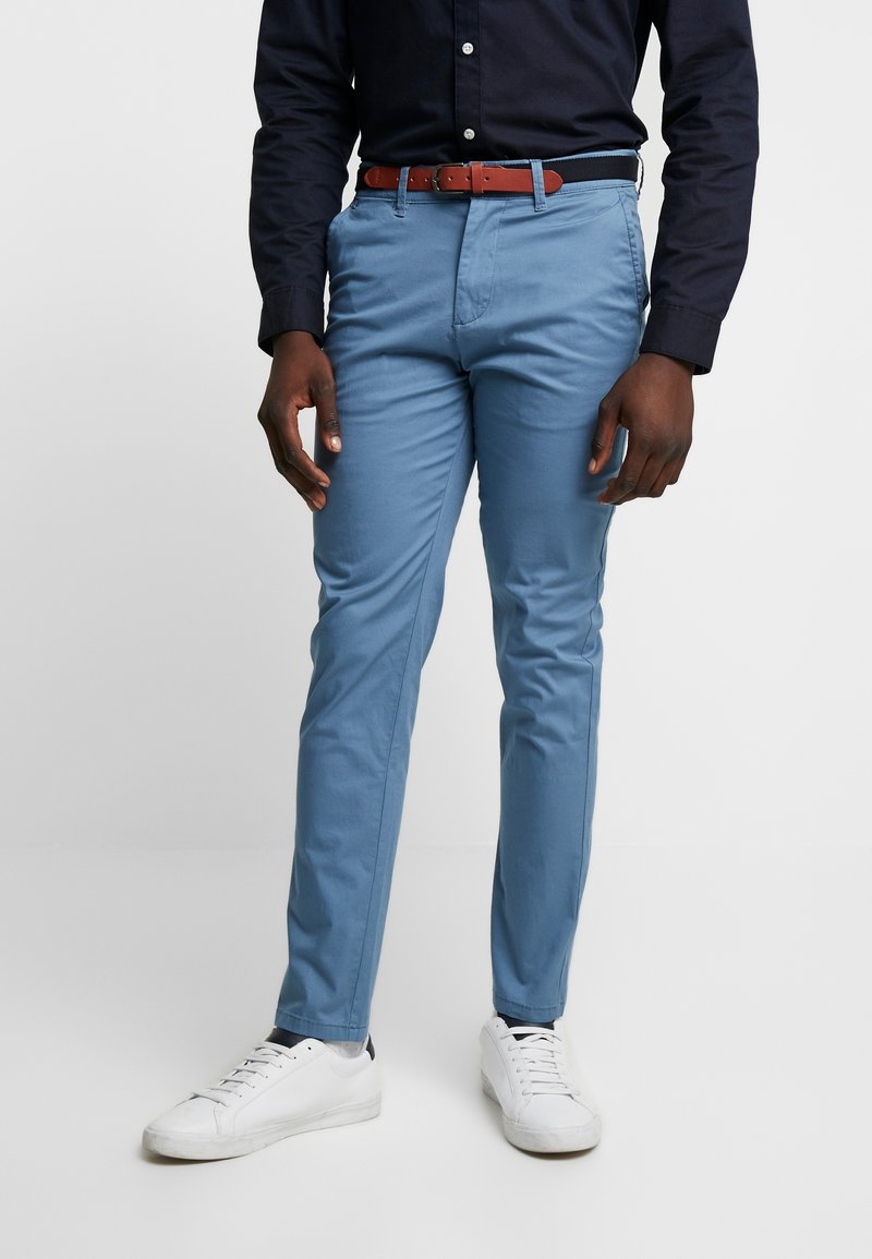 Světle modré chinos kalhoty s úzkým střihem, vyrobené z hladké bavlny. Kombinovány s hnědým koženým opaskem a bílými teniskami. Design s plochým předním dílem.