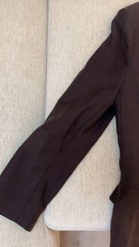 Manica di capo nero a manica lunga poggiata su una superficie di tessuto beige chiaro, che mostra una texture liscia e cuciture visibili.