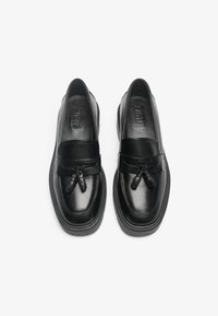 Schwarze Lederloafer mit glatter Oberfläche, featuring eine Schleifenakzent an der Vorderseite und einer dicken Sohle. Branding auf der Innensohle sichtbar.