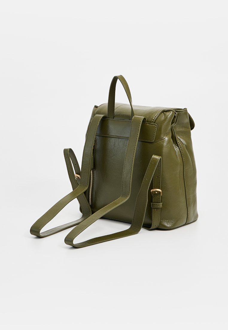 Grüner Leder-Rucksack mit glatter Textur, rechteckiger Form, umklappbarem Deckel, verstellbaren Trägern und einer mit Reißverschluss versehenen Rückentasche.