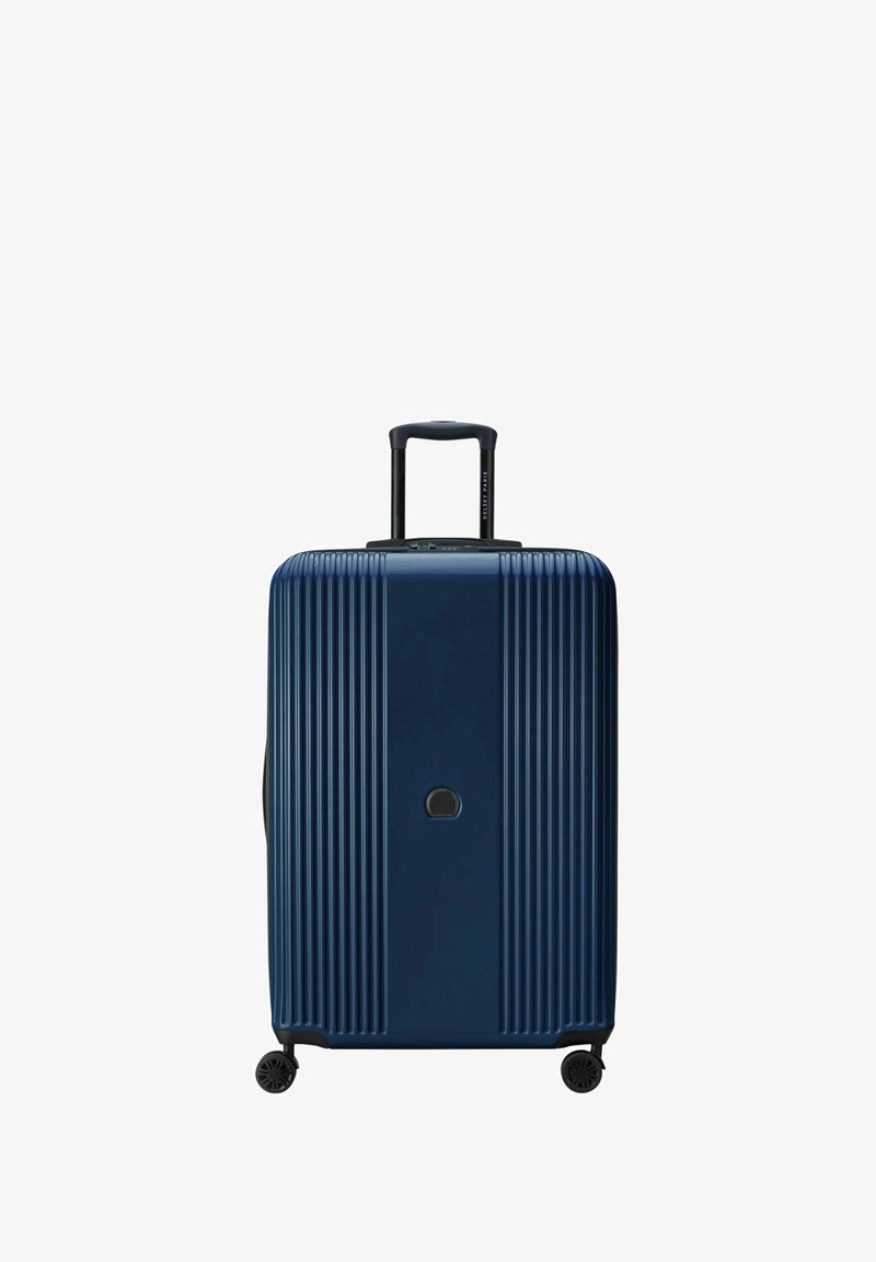 Valigia rigida blu navy con scanalature verticali, manico estraibile, doppie ruote e chiusura centrale con zip. Presenta un logo discreto sul davanti.