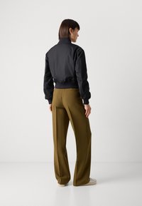Giacca bomber nera con polsini a coste, abbinata a pantaloni larghi color verde oliva. Texture liscia e dettagli di design minimali.
