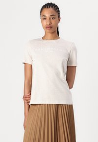 Light beige cotton t-shirt with short sleeves, featuring a white logo print "TOMMY HILFIGER EST 1985" on the front.