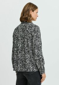 Blusa a maniche lunghe in un motivo astratto bianco e nero, con dettaglio arricciato sul retro e vestibilità ampia. Tessuto morbido con una texture liscia.