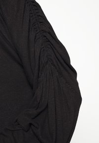 Svart skjorta med rynkat tyg på ärmen. Tillverkad av mjukt, strukturerat material med en flytande fall.