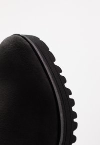 Stivale alla caviglia in suede nero con punta arrotondata e una suola spessa e testurizzata caratterizzata da un battistrada profondo per garantire aderenza. Dettagli di cucitura a contrasto sottili.