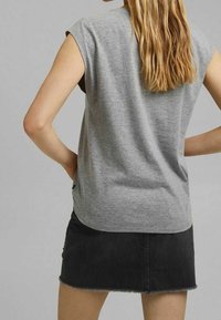 Grijze kortarmige top van zachte stof, met een ontspannen pasvorm en een ronde zoom, gecombineerd met een zwarte denim rok met rafelige randen.