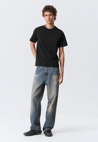 Black cotton t-shirt paired with faded blue wide-leg jeans. Model wears black sneakers. Simple design, short sleeves, comfortable fit.
