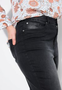 Jeans de mezclilla negra con un corte ajustado y bolsillos, con una textura suave y detalles de botones metálicos, combinados con una blusa de patrón floral.