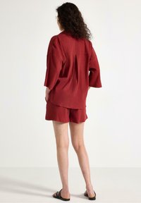 Röd strukturerad bomullsskjorta med kort ärm och matchande shorts, med en avslappnad passform och en veckdetalj bak.