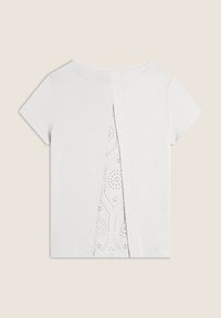 T-shirt bianco a maniche corte con uno spacco sul retro che rivela un tessuto a fantasia simile pizzo sottostante. Texture liscia e vestibilità comoda.