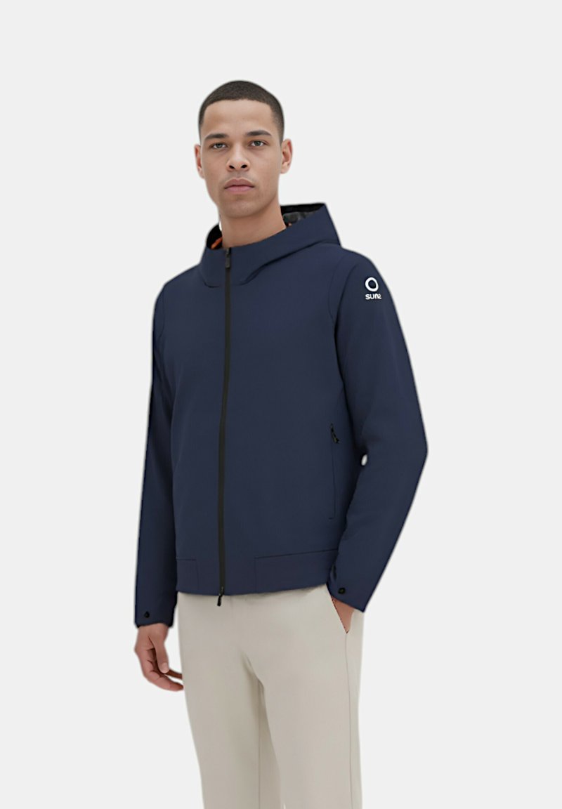 Giacca con cappuccio in navy con chiusura a zip e due tasche frontali. Presenta un interno a contrasto e un accento con logo sulla spalla sinistra. Tessuto liscio.