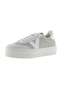 Zapatilla blanca con una parte superior de malla texturizada, acentos de gamuza y una suela elevada. Presenta cordones planos y un logotipo prominente en el costado.