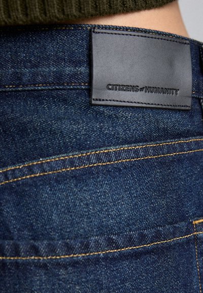 Dunkelblaue Denimjeans mit einem Lederpatch, das mit "CITIZENS of HUMANITY" beschriftet ist, und kontrastierenden gelben Nähten am Bund.
