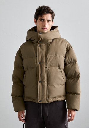 Brown padded jacket with a high collar and oversized hood, featuring snap buttons and two front pockets, made from a smooth fabric.