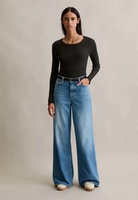 Svart ribbad långärmad topp ihop med vida ljusblå denimjeans, med en klassisk femficksdesign och ett svart skärp.