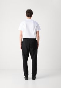Hvit t-skjorte med korte ermer, kombinert med sorte joggebukser med elastisk midjebånd og baklomme, brukt med sorte sko.