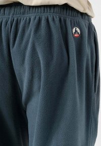 Close-up van donkerblauwe fleece broek met elastische tailleband en een klein gestikt logo op de bovenbenen.